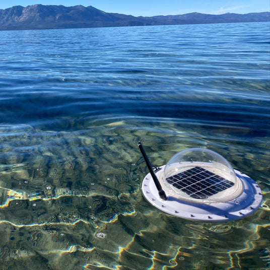 Solar-powered lake water monitoring device floating on clear lake with mountains in background